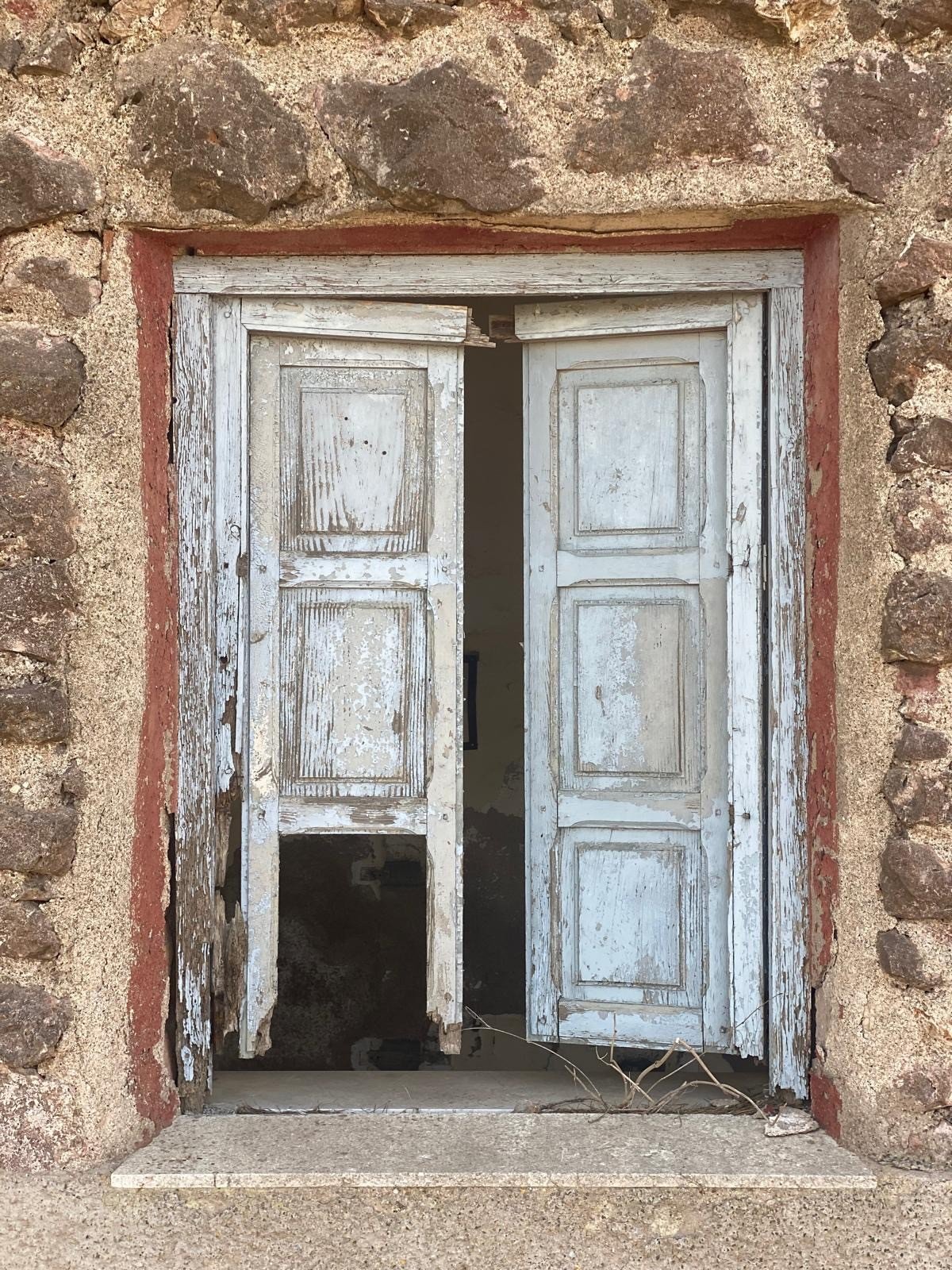 Weathered white wooden double door in a wall of rough natural stone at the coastal battery