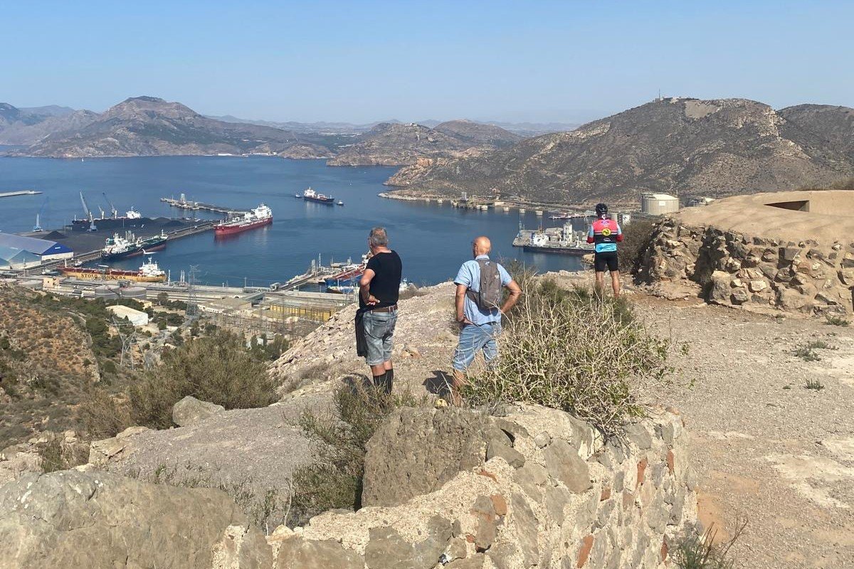 Walkers and a cyclist at a viewpoint along the route, with the port of Escombreras and the bay below