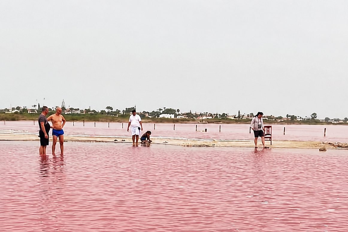 Das rosa Wasser der Laguna Salada de Torrevieja mit Besuchern am Rand der Salzfl&auml;che