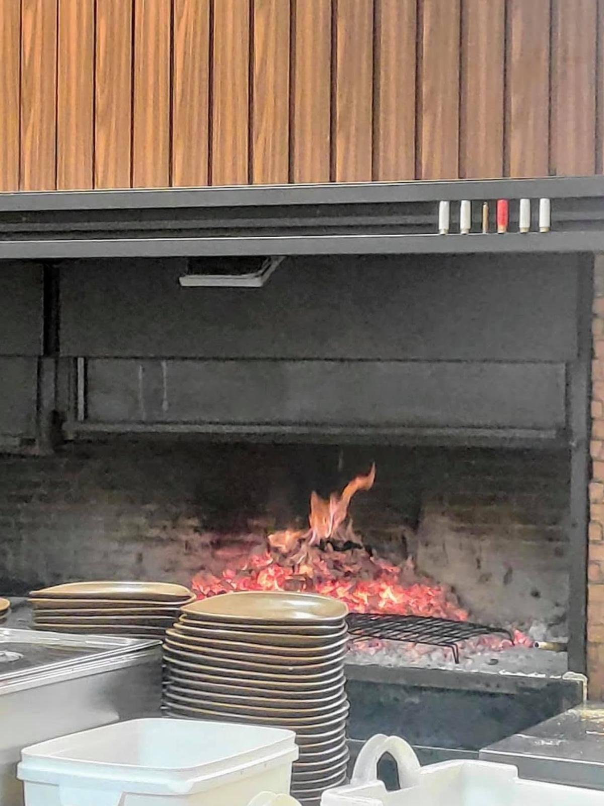 Offener Holzkohlegrill mit gl&uuml;hender Glut und Tellerstapeln im Restaurante El Patio
