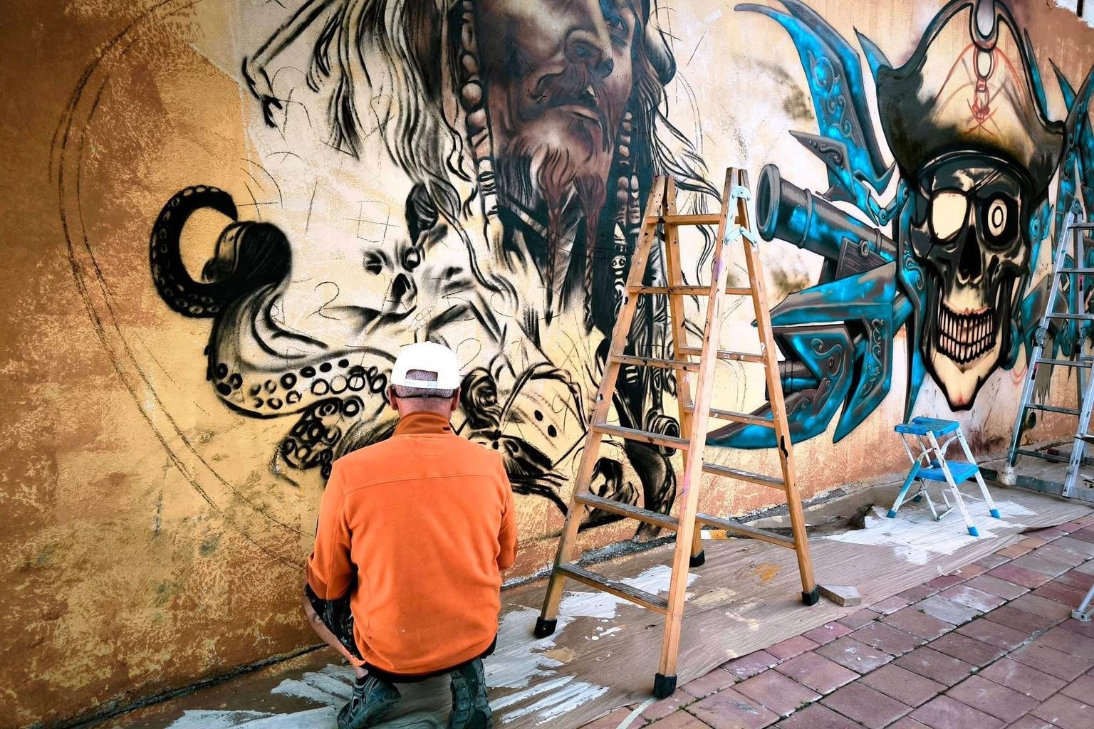 Zwei K&uuml;nstler arbeiten mit Leitern an einem gro&szlig;en Wandbild mit Piratenmotiv