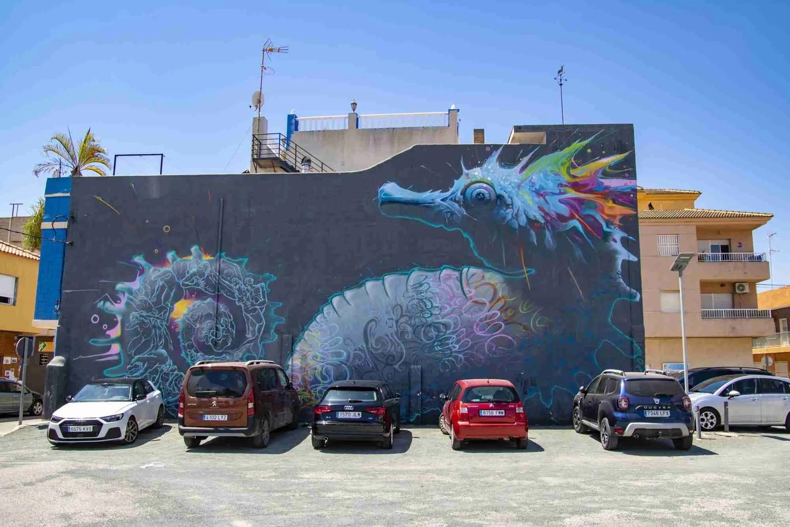 Wandbild eines Seepferdchens an einer dunklen Fassade neben einem Parkplatz