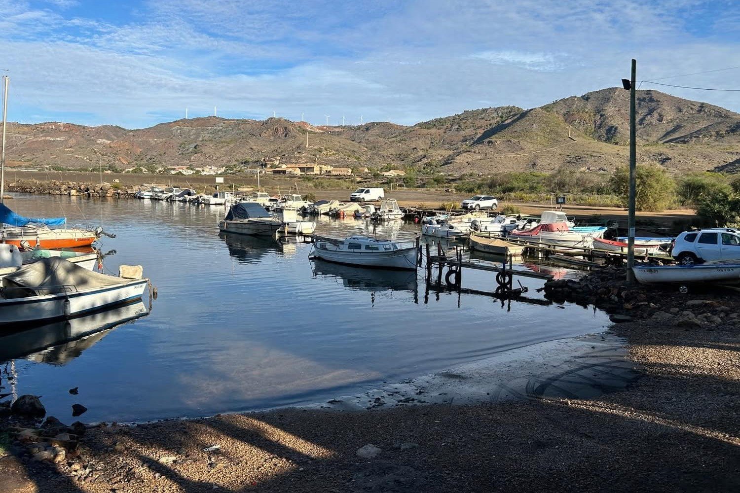 Kleiner Sporthafen mit Fischerbooten in Portm&aacute;n, mit dunklem Sand und den Bergbauh&uuml;geln dahinter