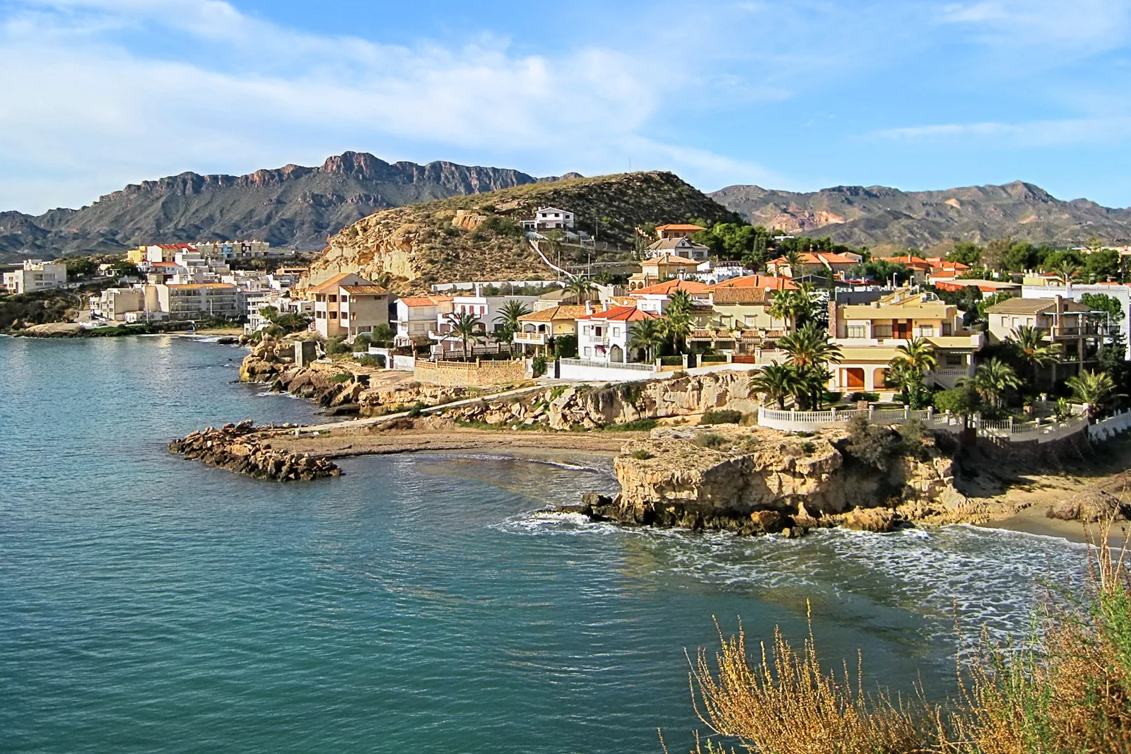 De kust en bebouwing van San Juan de los Terreros, gezien vanaf een rotsachtige baai