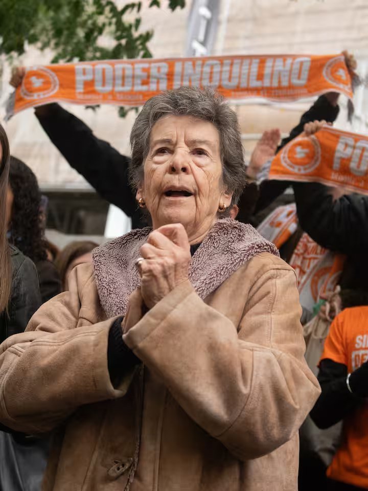 Ältere Frau zwischen Demonstranten mit orangefarbenen Schals der Mieterbewegung Poder Inquilino in Madrid